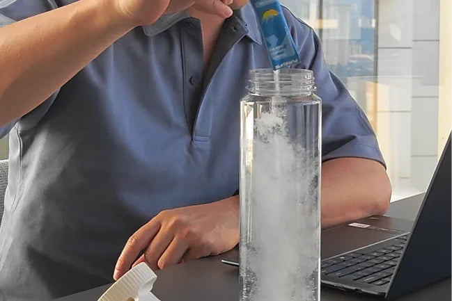 Person mixing an electrolyte drink in water while working at a desk